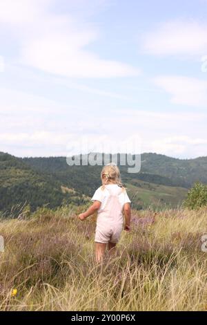 Niedliches kleines Mädchen, das auf einer Wiese in der Nähe von Bergen steht, Rückansicht Stockfoto