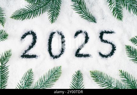 Trendiges Weihnachtslayout mit grünen, verschneiten Weihnachtsbaumzweigen und 2025 Jahre in Schnee geschrieben. Kreativer Winterhintergrund. Neujahrskonzept. Stockfoto