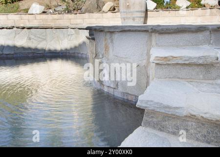 Blick auf einen Swimmingpool mit Steintreppe und Mini-Wasserfall. Stockfoto