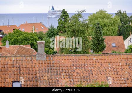 Blick auf Dachziegel, viele Bäume und Schornsteine, ein großes Schiff im Hintergrund und das Meer, svaneke, bornholm, ostsee, dänemark, skandinavien Stockfoto