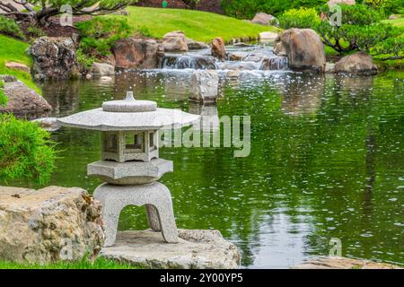 Eine Steinlaterne am Rande eines Teichs im Nikka Yuko Japanischen Garten in Lethbridge, Alberta Stockfoto