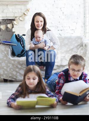 Sohn und Tochter mit Mutter und Bruder, die auf dem Sofa sitzen. Kinder lesen Bücher im Wohnzimmer. Konzentrieren Sie sich auf Frau und Baby Stockfoto