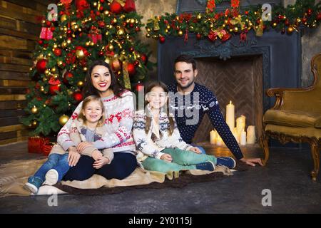 Junge Familie mit zwei Kindern am Kamin feiert Weihnachten. Liebes- und Beziehungskonzept Stockfoto