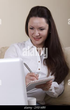 Junge Geschäftsfrau, die auf Papier schreibt, neben dem Laptop Stockfoto