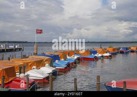 Mehrere Boote parken entlang einer Anlegestelle an einem See und teilweise mit farbigen Planen umhüllt, oberhalb eines bewölkten Himmels, Bad Zwischenahn, Zwischenahner Meer, A Stockfoto