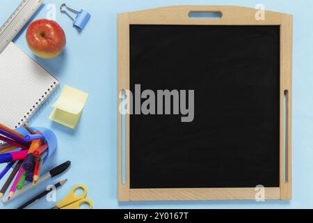 Flat Lay mit Schulkonzept auf blauem Hintergrund mit verschiedenen Schulzubehör, Stiften, Bleistift, Notizblock, Büroklammern, apfel, Lineal, Schere, leer Stockfoto