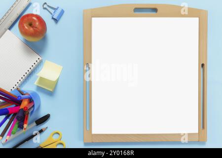 Flat Lay mit Schulkonzept auf blauem Hintergrund mit verschiedenen Schulzubehör, Stiften, Bleistift, Notizblock, Büroklammern, apfel, Lineal, Schere, leer Stockfoto