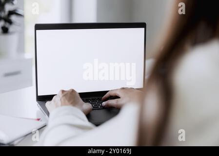 Weibliche Hände tippen auf dem Laptop mit leerem weißen Bildschirmmodell. Der Computer liegt auf dem weißen Tisch. Unscharfer Hintergrund. Person, von der aus gearbeitet wird Stockfoto