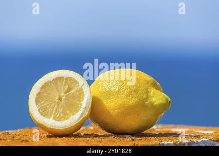 Ganze und halbe gelbe Zitrone mit blauem Himmel und Meer Stockfoto