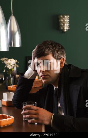 Junger Mann im Anzug, der an einer Bar sitzt und Alkohol trinkt Stockfoto