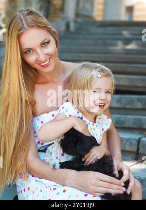 Niedliche kleine Mädchen und ihre Mutter umarmt Hund Welpen. Freundschaft und Pflege-Konzept Stockfoto