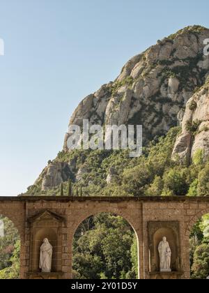 Statuen, die in Steinbögen vor einer markanten, grünen Felsenlandschaft unter blauem Himmel integriert sind, montserrat, spanien Stockfoto