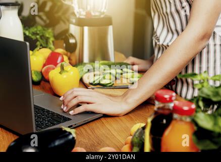 Junge Frau, die einen Laptop benutzt, Mädchen mit der Hand klickend, pc berührend. Person, die nach Rezepten sucht oder Tutorial ansieht. Frisches Essen auf dem Tisch in der Küche. Co Stockfoto