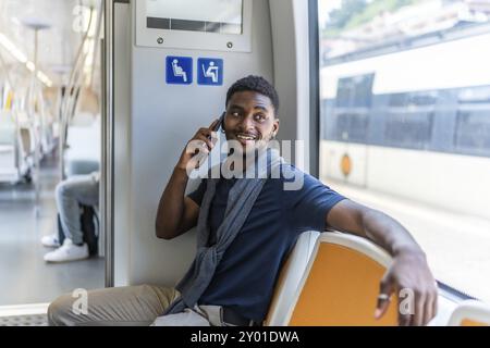 Intelligenter afrikanischer Geschäftsmann, der auf der Metro sitzt und mit dem Handy neben dem Fenster spricht Stockfoto