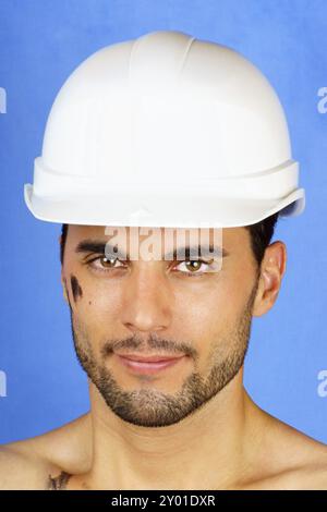 Porträt von einem schmutzigen Arbeiter mit Schutzhelm vor einem blauen Hintergrund Stockfoto