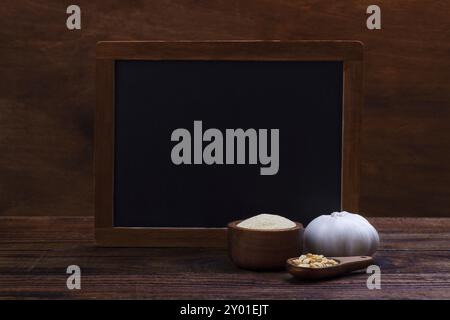 Knoblauchzehen, Knolle, Flocken und Pulver auf altem hölzernem Hintergrund mit schwarzer Tafel für Text Stockfoto