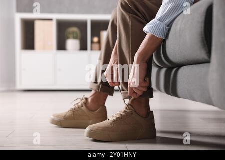 Mann, der drinnen einen Schnürsenkel auf dem Sofa bindet, Nahaufnahme Stockfoto