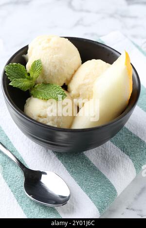 Löffel leckeres Melonensorbet mit Minze in Schüssel und Löffel auf weißem Tisch, Nahaufnahme Stockfoto