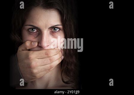 Nahaufnahme einer Hand, die einen Frauenmund bedeckt. Konzept häuslicher Gewalt oder Entführung. Dunkle Stimmung Stockfoto