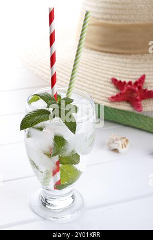 Erfrischendes Sommergetränk, kohlensäurehaltiges Wasser mit Eis und Minze mit Strandaccessoires auf weißem Holzbrett. Selektiver Fokus Stockfoto