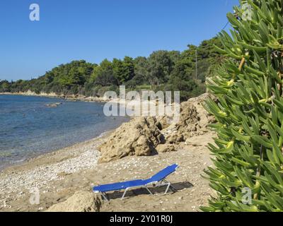 Eine blaue Liege am Strand, umgeben von Felsen und Pflanzen mit Blick auf das Meer, katakolon, mittelmeer, griechenland Stockfoto