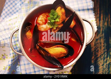 Draufsicht auf eine Schüssel köstlicher Suppe mit Garnelen und Muscheln, die in der Nähe von Serviette auf dem Tisch im Restaurant platziert werden Stockfoto