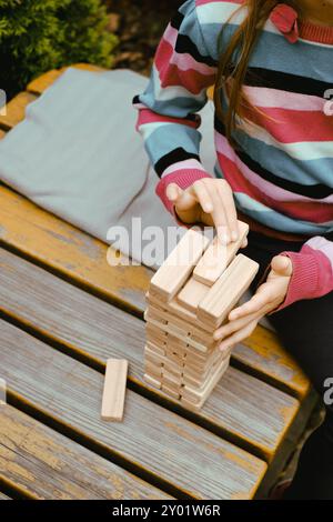 Person, die Holzblöcke stapelt, Turm baut, während sie an einem Tisch im Freien sitzt, konzentriert sich auf das Ausbalancieren der Teile. Nahaufnahme Stockfoto