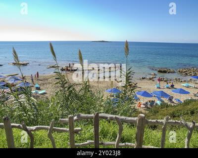 Strand mit Sonnenschirmen und Liegestühlen, Blick auf das ruhige Meer und eine kleine Insel am Horizont, katakolon, mittelmeer, griechenland Stockfoto