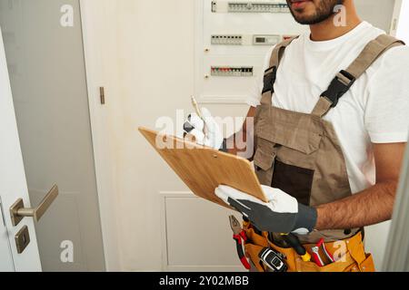 Nahaufnahme eines männlichen Elektrikers überprüft den Stromverteiler und schreibt auf dem Tablet Stockfoto