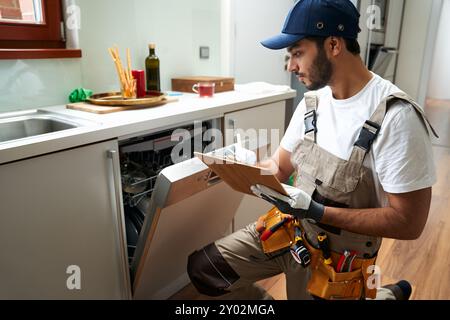 Servicemitarbeiter, der in der Nähe des Geschirrspülers sitzt und in der Küche auf das Klemmbrett schreibt. Hochwertige Fotos Stockfoto