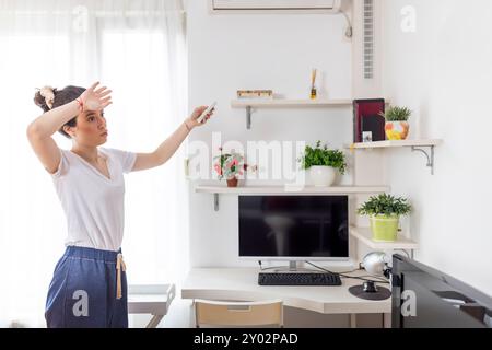 Die junge Frau passt die Temperatur der Klimaanlage mit der Fernbedienung im Zimmer zu Hause an Stockfoto