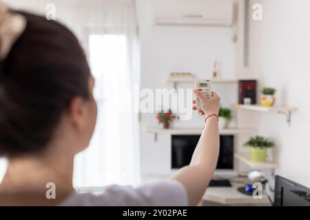 Die junge Frau passt die Temperatur der Klimaanlage mit der Fernbedienung im Zimmer zu Hause an Stockfoto