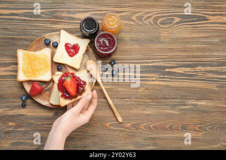 Frau mit köstlichem Toast mit Erdbeermarmelade und Beeren auf braunem Holzhintergrund Stockfoto