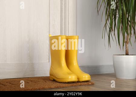 Gelbe Gummistiefel auf der Matte in der Nähe der Tür Stockfoto