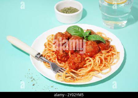 Teller mit gekochter Pasta mit Tomatensoße und Fleischbällchen auf blauem Hintergrund Stockfoto