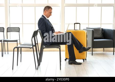 Reifer Geschäftsmann mit Laptop in der Halle des Flughafens Stockfoto