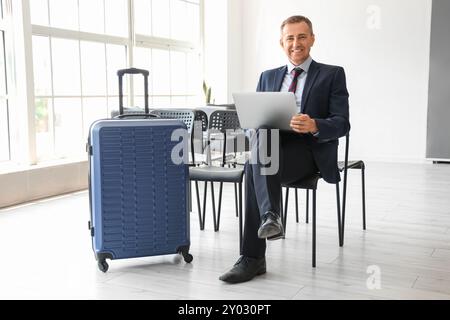 Reifer Geschäftsmann mit Laptop in der Halle des Flughafens Stockfoto