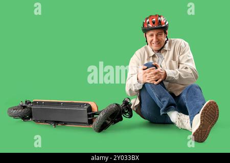 Reifer Mann mit Helm fiel vom Elektroroller auf grünem Hintergrund Stockfoto