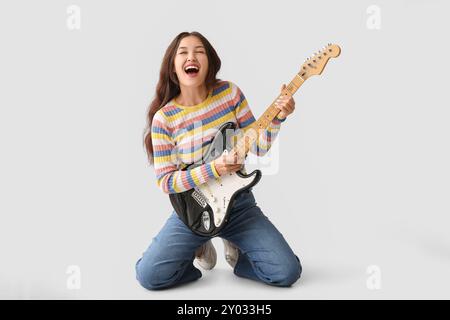 Junge Frau, die elektrische Gitarre spielt und auf grauem Hintergrund singt Stockfoto