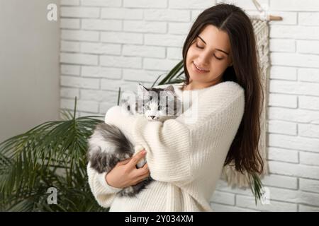 Junge Frau, die zu Hause niedliche langhaarige Katze hält Stockfoto