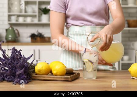 Junge Frau, die Zitronensaft aus der Kanne in Glas gießt, um Lavendellimonade am Tisch in der Küche zuzubereiten Stockfoto