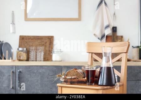 Krug und Glas leckerer Kwass mit Brotscheiben, Spikelets auf Stuhl in der Küche Stockfoto