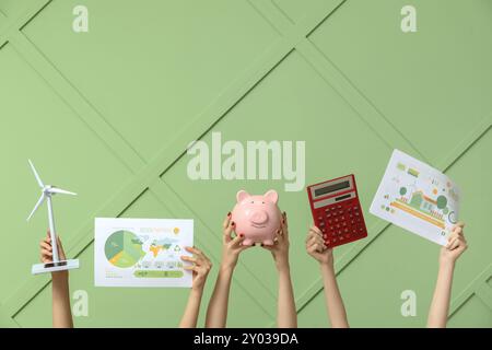 Viele Hände mit Windturbinenmodell, Schweinebank und Diagrammen auf farbigem Hintergrund. Konzept der grünen Energie Stockfoto