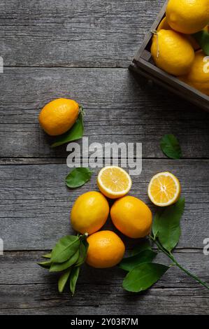 Frische reife gelbe Zitronenfrüchte mit Blättern auf hölzernem Hintergrund Stockfoto