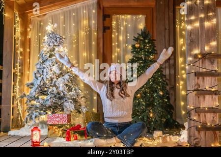 Christmas Lights Frau Veranda festliche Dekor - Eine Frau sitzt auf einer Veranda mit Weihnachtsbeleuchtung und Bäumen und feiert die Weihnachtszeit. Stockfoto