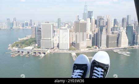 New York City schließt Hubschrauberflüge ab, Helikopterflüge über Manhattan Downtown, USA. World Trade Center. Füße in Turnschuhen, Touristenbeine, Schuhe Selfie pov. Extreme Reisen USA. Kamera schüttelt. Stockfoto