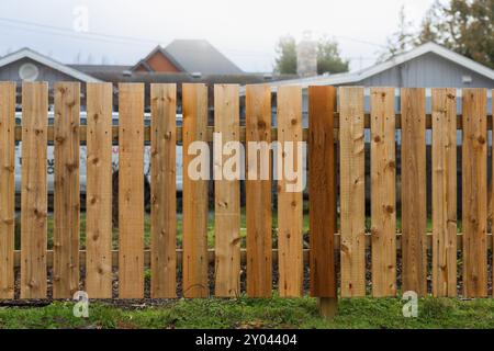 Großer neuer Holzzaun um das Haus und die Bäume. Holzzaun mit grünen Bäumen. Zäune und Tore. Hochwertiger Zaun. Straßenfoto Stockfoto