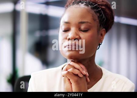 Spirituelle afroamerikanische Frau, die von Gott durch Gebet in ihrem Amt Führung sucht und über ihren christlichen Glauben nachdenkt. Stockfoto