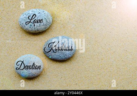 Blick von oben auf Liebe, Freundlichkeit und Hingabe Joy Text auf Steine mit Sandhintergrund am Strand graviert. Positives Vibe-Konzept. Stockfoto