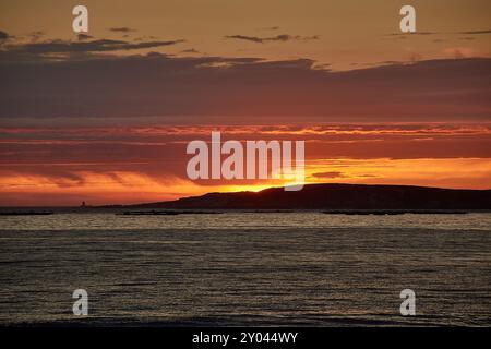 Ein roter Sonnenuntergang über Playa América in Nigrán, Spanien, mit der Silhouette der Las Estelas Inseln im Hintergrund. Der Himmel ist in tiefen Tönen gemalt Stockfoto